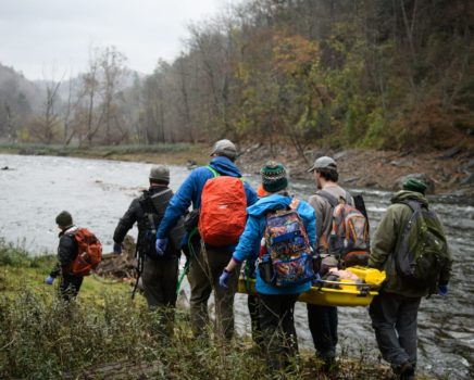 Group of people carrying a person in a stretcher by a river on the AWFA-WFR Bridge Course