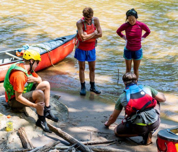 four paddlers standing by canoes