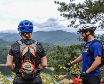 two mountain bikers look out over fontana lake with mountains in the background
