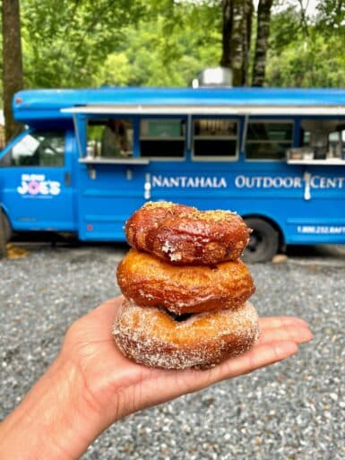 Hand holding up delicious donuts in front of an awesome food truck.